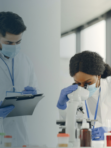 Due ricercatori che analizzano al microscopio e prendono appunti