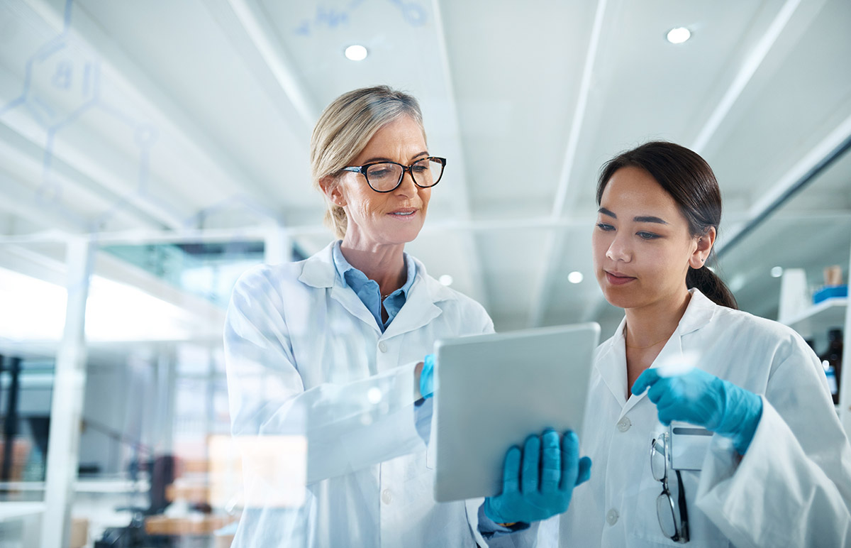 Women, scientist and discussion in laboratory with tablet, reading and review with results at pharma company. People, mentor and feedback with solution, board and medical research for mpox vaccine.