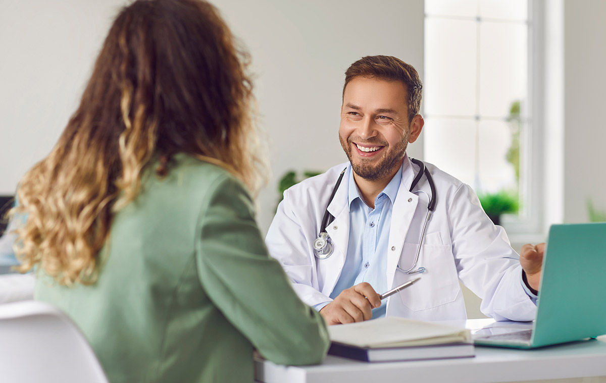 Conversation with doctor. Portrait of friendly male doctor happily listening to his female patient in medical office. Medic looks at woman in front of him. Concept of medicine, healthcare and people.